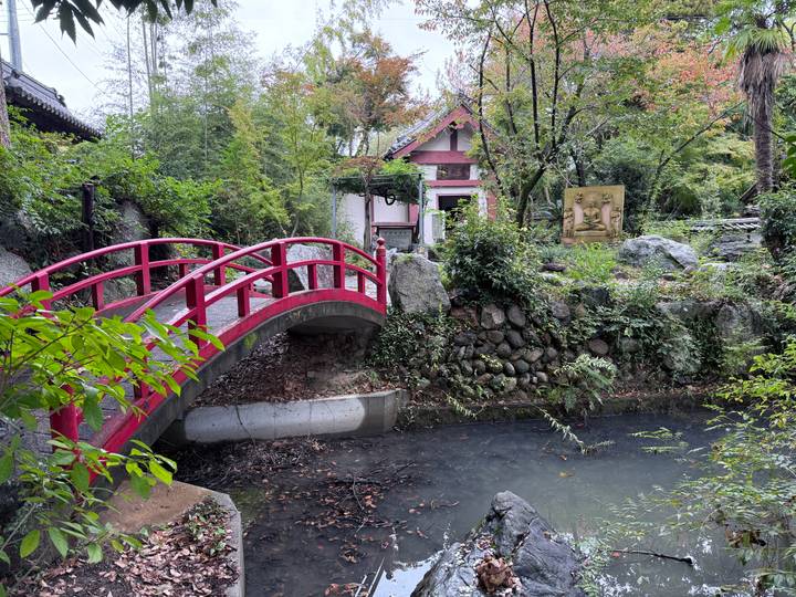 Red footbridge over a stream in a tranquil garden.