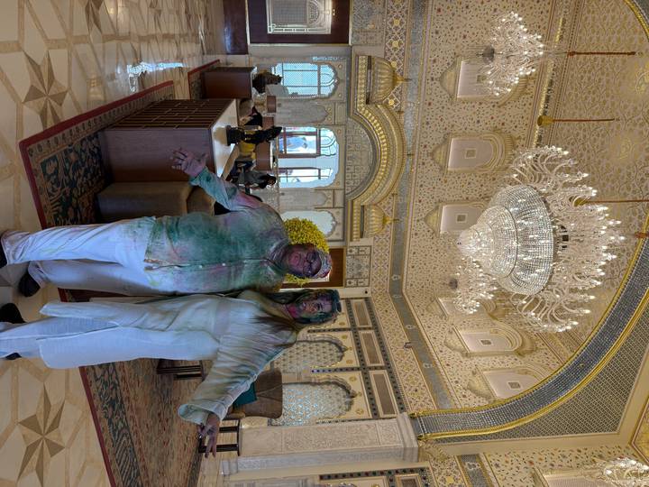 Two people covered in color pigment inside an ornate building.