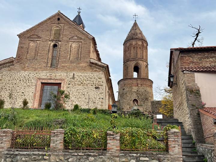 Iglesia histórica con torre redonda en una colina cubierta de hierba.