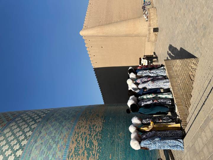 Personas con vestimenta tradicional de pie frente a un minarete.