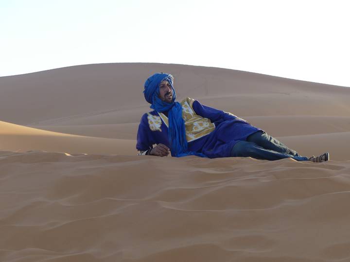 Person in traditional attire laying on sand dunes.