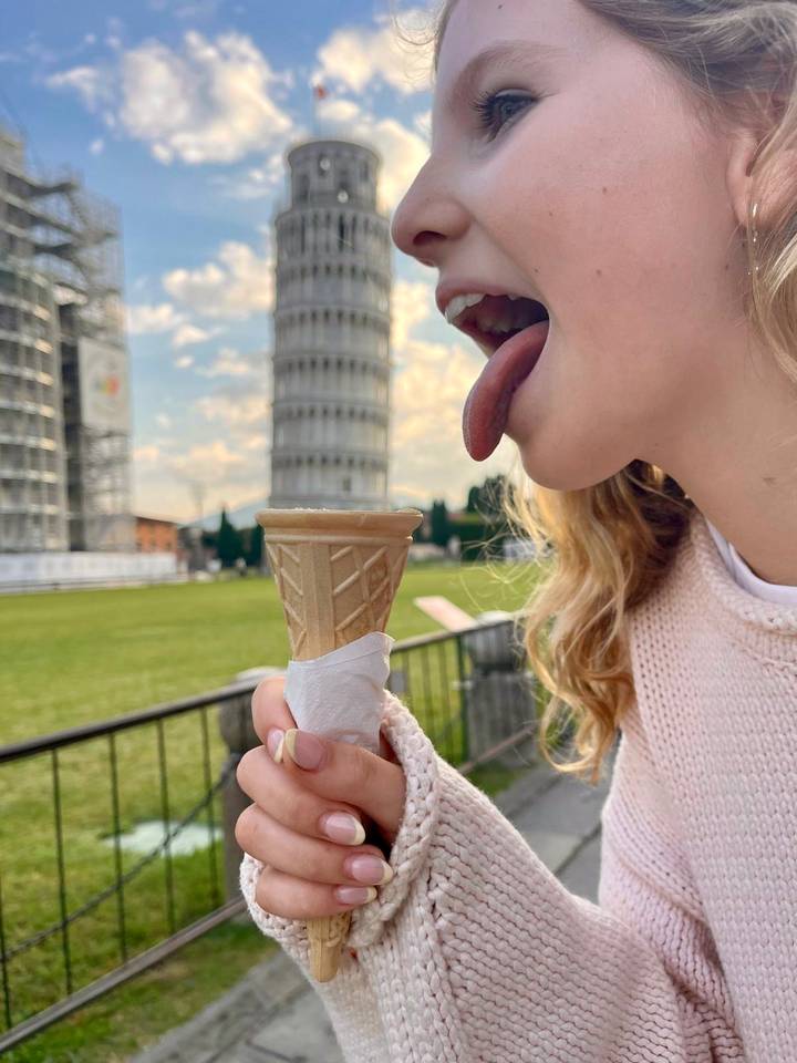 Person, die humorvoll vorgibt, den Schiefen Turm von Pisa zu lecken.