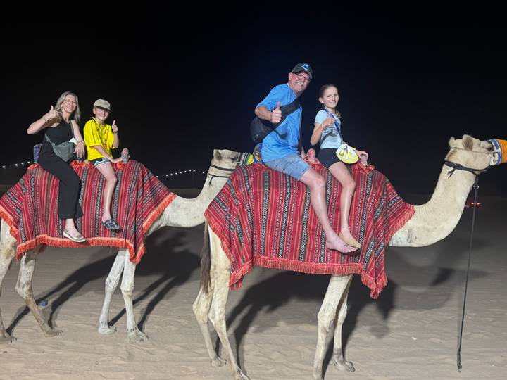 Familie reitet nachts auf Kamelen in einer Wüstenlandschaft.