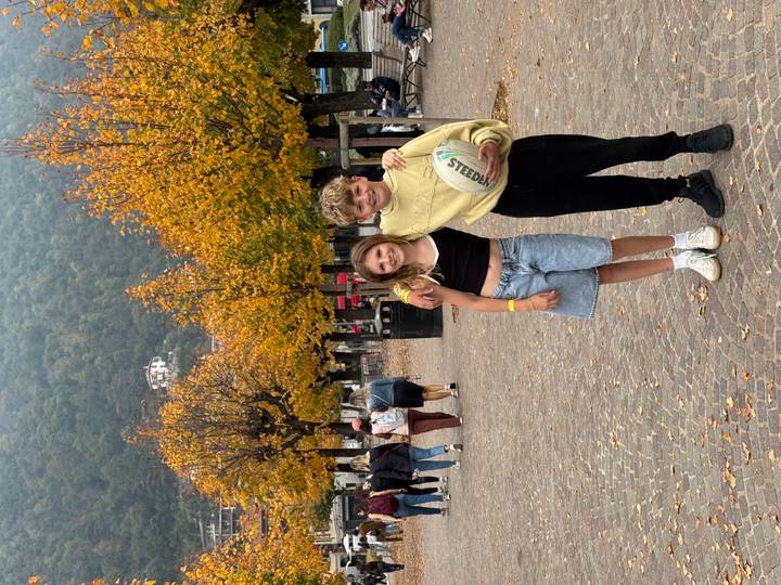 Zwei Kinder posieren mit Herbstbäumen im Hintergrund.