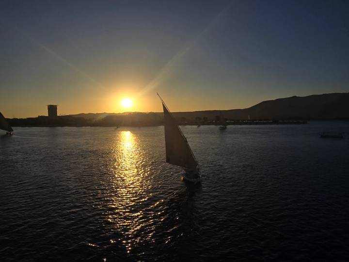 Velero en un río al atardecer con colinas.