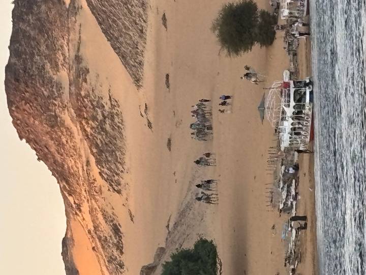 Mensen die op kamelen rijden op zandduinen bij een rivier.