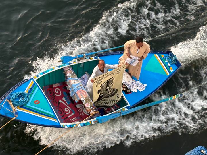 Twee mannen op een kleine boot die textiel verkopen op een rivier.