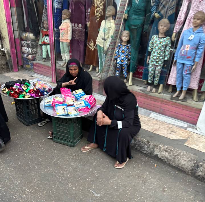 Vrouwen zittend op straat, goederen verkopend op een markt.