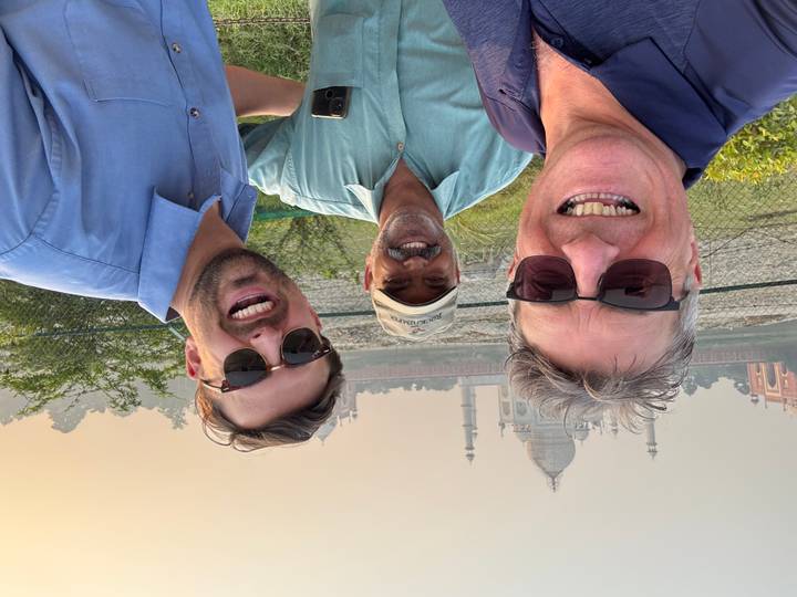 Drei Männer lächeln mit dem Taj Mahal im Hintergrund.