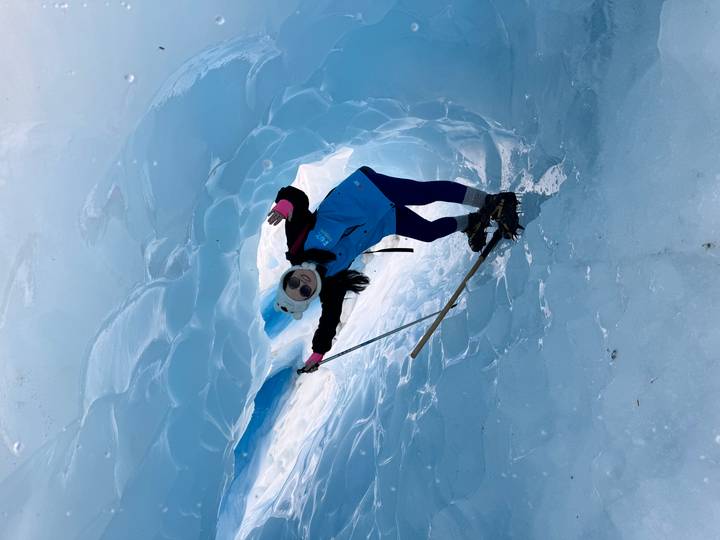 Persoon die een blauwe ijsgrot verkent met een ijsbijl