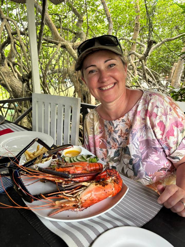 Mujer sonriendo con un plato de mariscos en un restaurante.