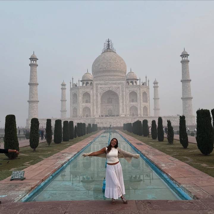 A person posing in front of the Taj Mahal in the morning mist.
