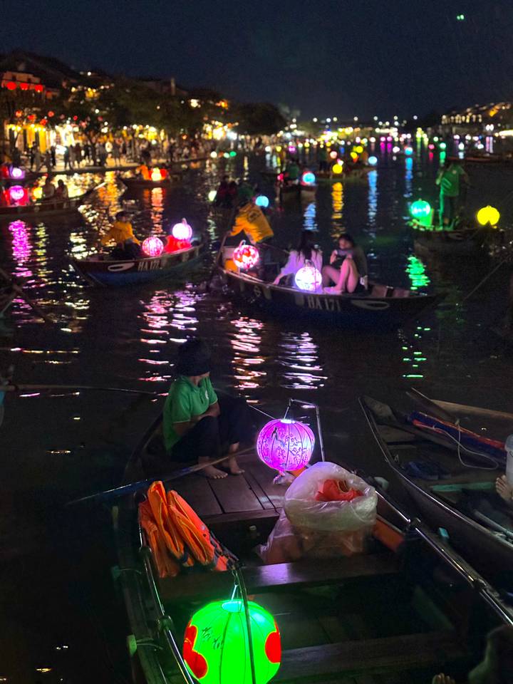 Mensen in boten met kleurrijke lantaarns in de nacht.