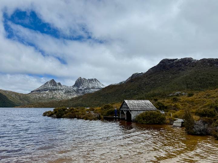 Una casa de botes junto al agua con montañas cubiertas de nieve al fondo.