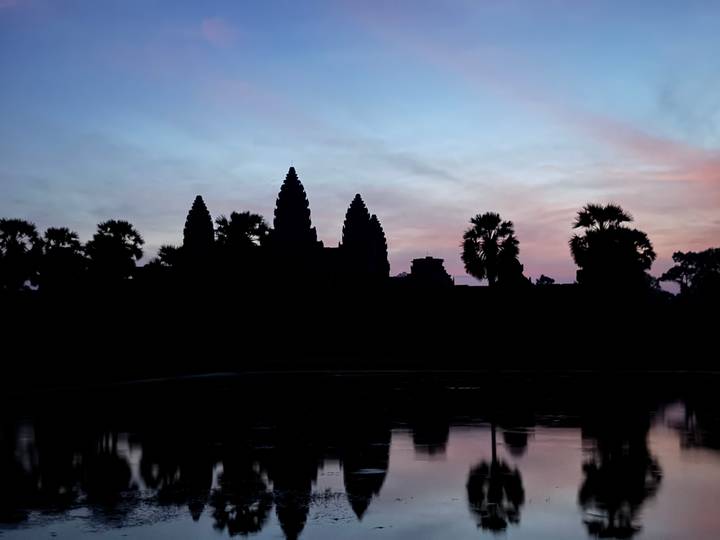 Silhouet van Angkor Wat bij zonsopgang, met een reflectie in een nabijgelegen waterpartij.