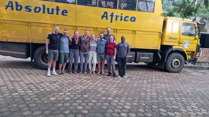 Grupo de personas posando frente a un camión amarillo con la etiqueta 'Absolute Africa'.