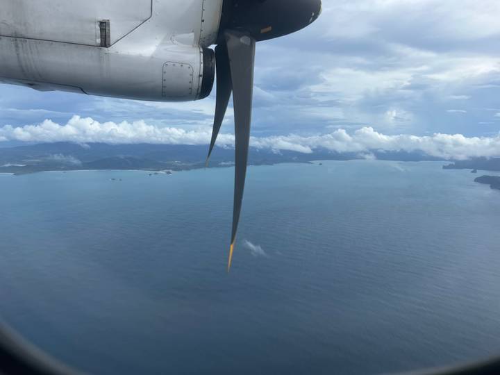 Luftaufnahme von Küstenlinie und Ozean mit sichtbarem Flugzeugtriebwerk.