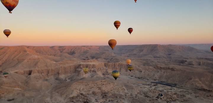 Heißluftballons, die bei Sonnenaufgang über eine Wüstenlandschaft aufsteigen.
