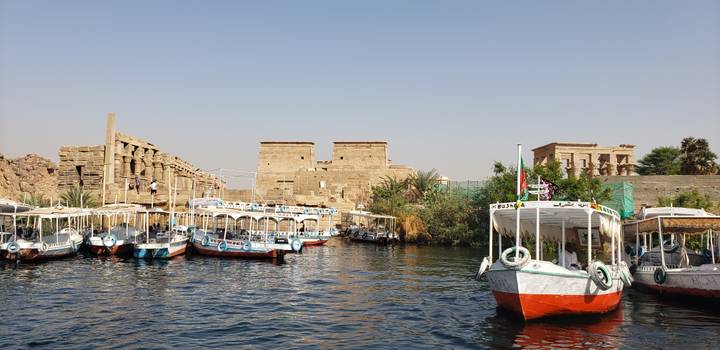 Boote auf dem Fluss vor antiken Tempeln mit Touristen.