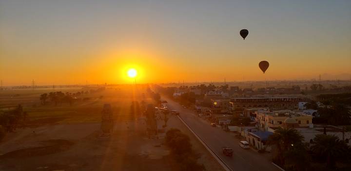 Sonnenuntergang über einer Stadt mit Heißluftballons am Himmel.