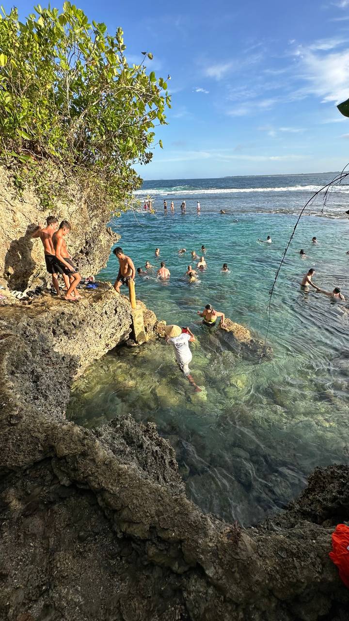 Menschen schwimmen und klettern auf Felsen in einem klaren Ozean.