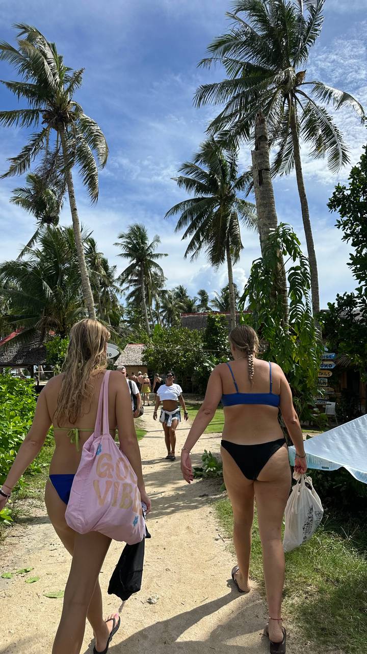 Rückansicht von zwei Frauen, die zu einem mit Palmen gesäumten Strand gehen.