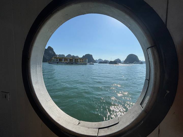 View from a ship's porthole capturing boats and karst landscapes.