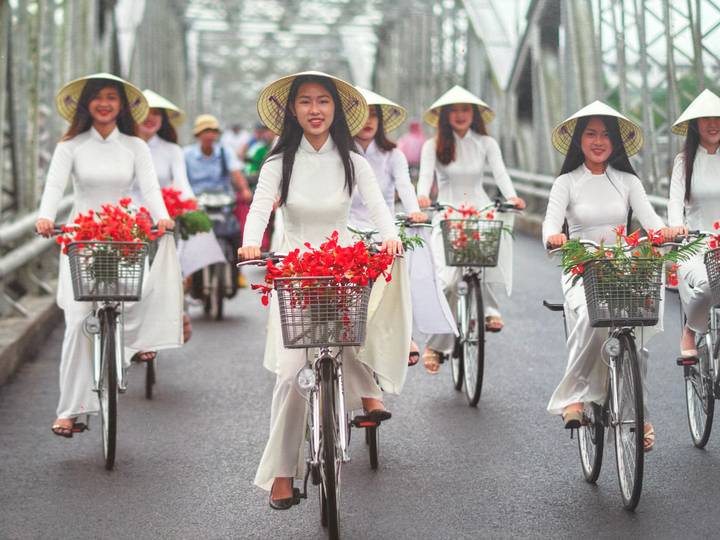 Women in traditional white dresses biking with flower baskets.