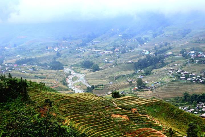 Weite Aussicht auf terrassenförmige Felder und Flüsse unter einem bewölkten Himmel.