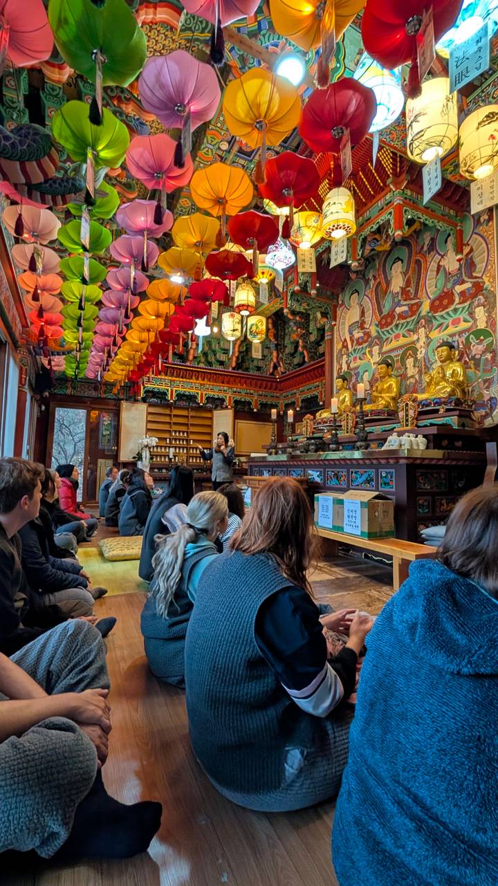 Menschen, die in einem traditionellen buddhistischen Tempel mit farbenfroher Dekoration sitzen.