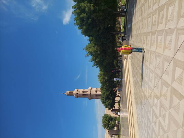 Un minarete alto y jardín con gente paseando alrededor.