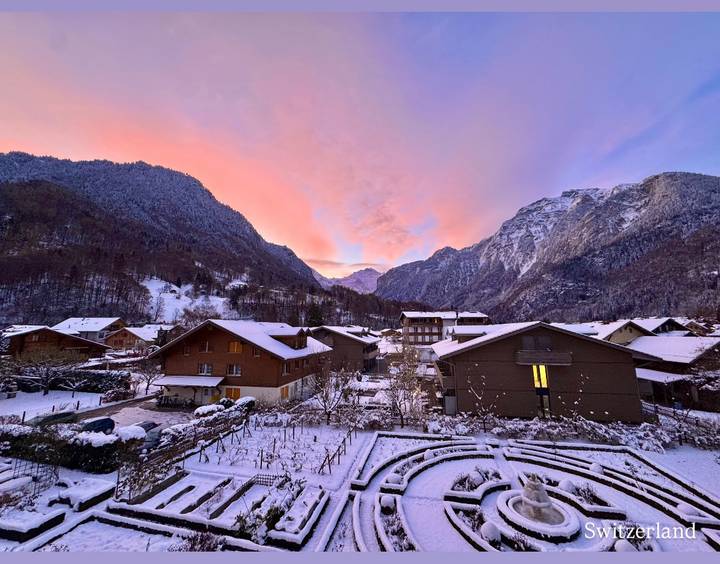 Snow-covered village with mountains in the background at sunrise.