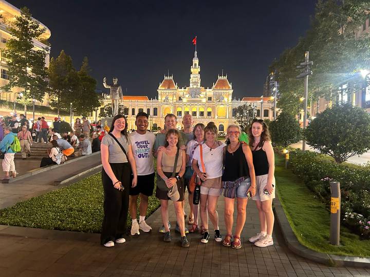 Gruppe von Touristen, die nachts vor einem beleuchteten historischen Gebäude posieren.