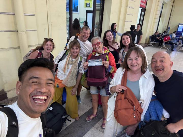 Gruppe von Touristen an einem Bahnhof, lächelnd und Fahrkarten haltend.