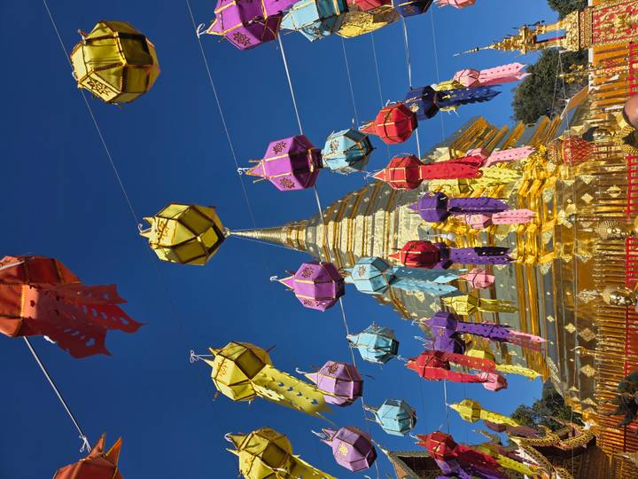 Goldener Tempel mit bunten Laternen vor einem klaren blauen Himmel.