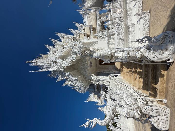 Weißer Tempel mit kunstvollen Schnitzereien und blauem Himmel.