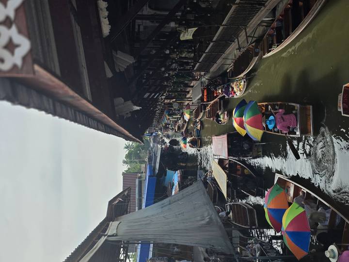 Geschäftiger schwimmender Markt mit bunten Sonnenschirmen auf Booten.