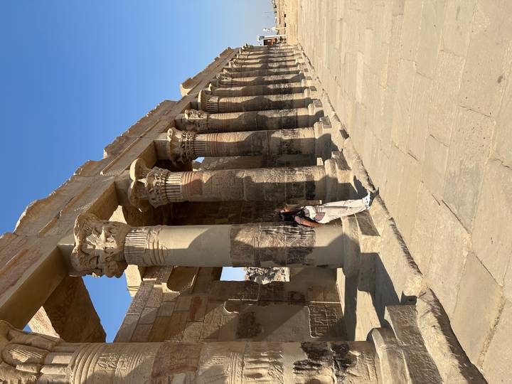 Persona posando contra columnas antiguas bajo un cielo azul.
