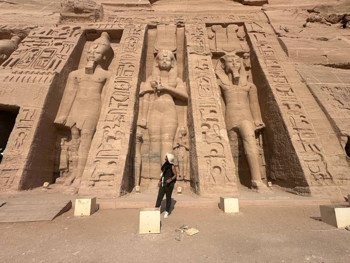 Persona de pie frente a estatuas colosales y jeroglíficos.