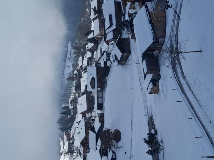 Verschneites Dorf mit Holzhäusern und einer bergigen Kulisse.