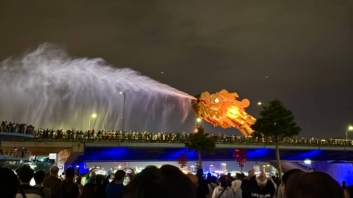 Multitud observando una escultura de dragón en un puente que arroja agua por la noche.