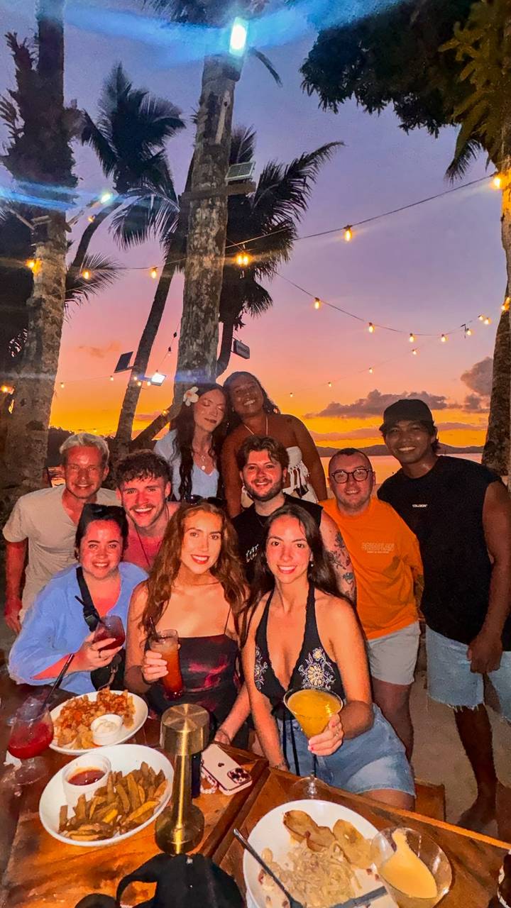 Eine Gruppe von Menschen, die einen tropischen Sonnenuntergang mit Lichterketten genießt.