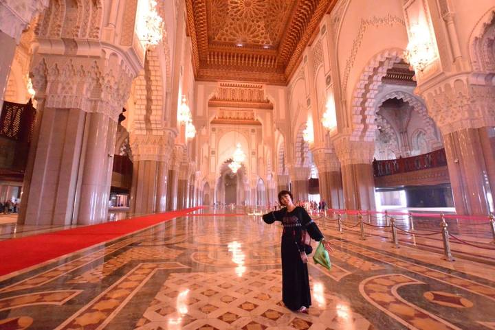 Interior of a grand mosque with chandeliers and red carpets.