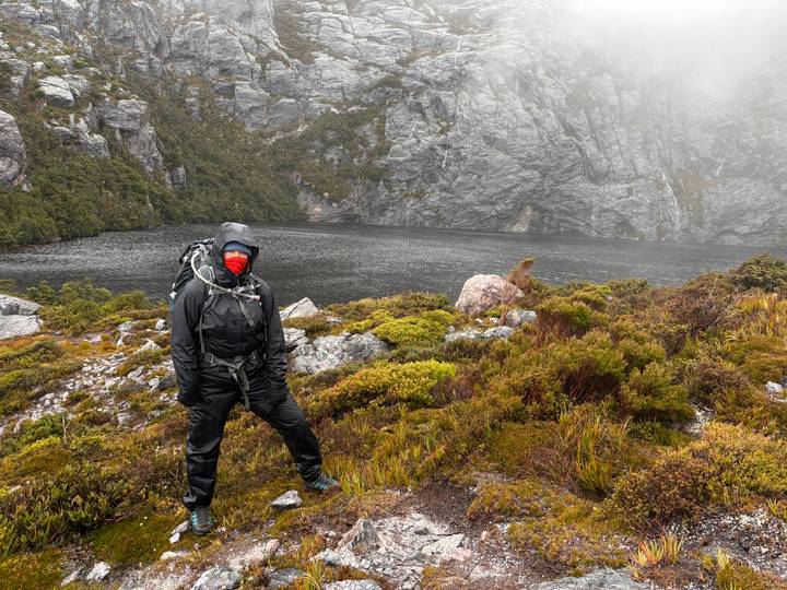 Excursionista de pie junto a un lago brumoso en un paisaje rocoso.