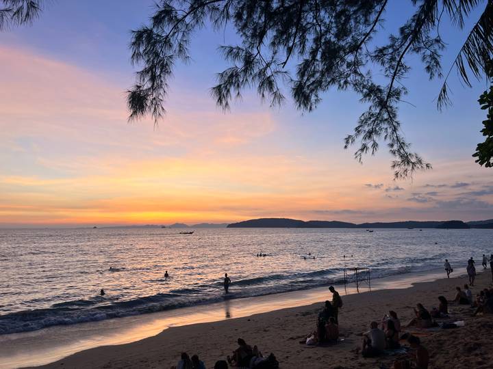 Playa durante la puesta de sol con personas nadando y relajándose.
