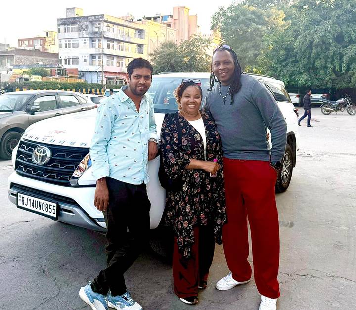 Drei Personen stehen vor einem Auto in einer städtischen Umgebung.