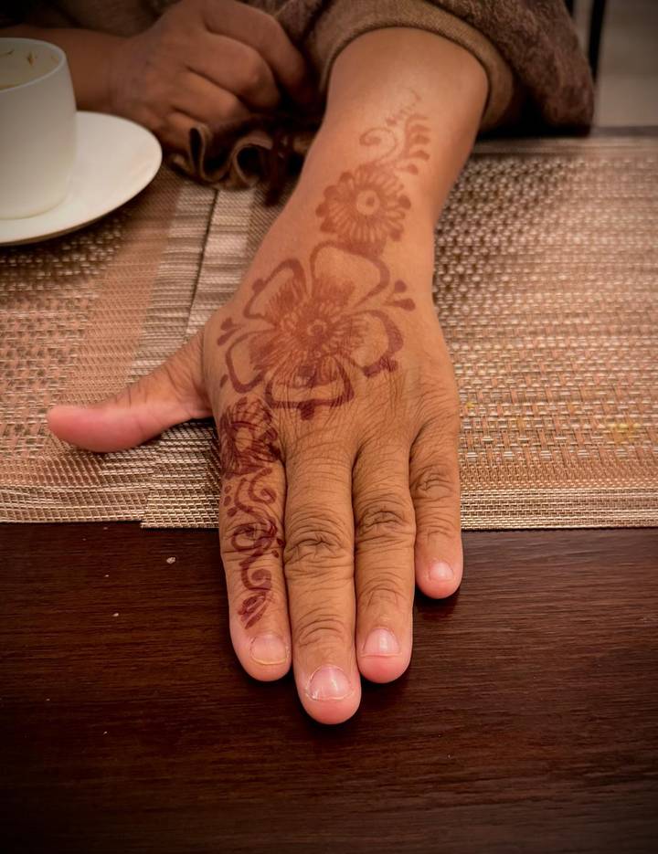 Nahaufnahme eines Henna-Designs auf der Hand einer Person, die auf einer strukturierten Oberfläche liegt.