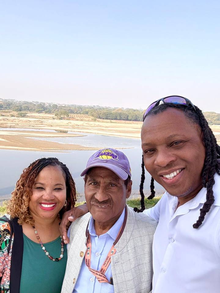 Drei Personen machen ein Selfie mit einer malerischen Aussicht auf einen Fluss oder See im Hintergrund.