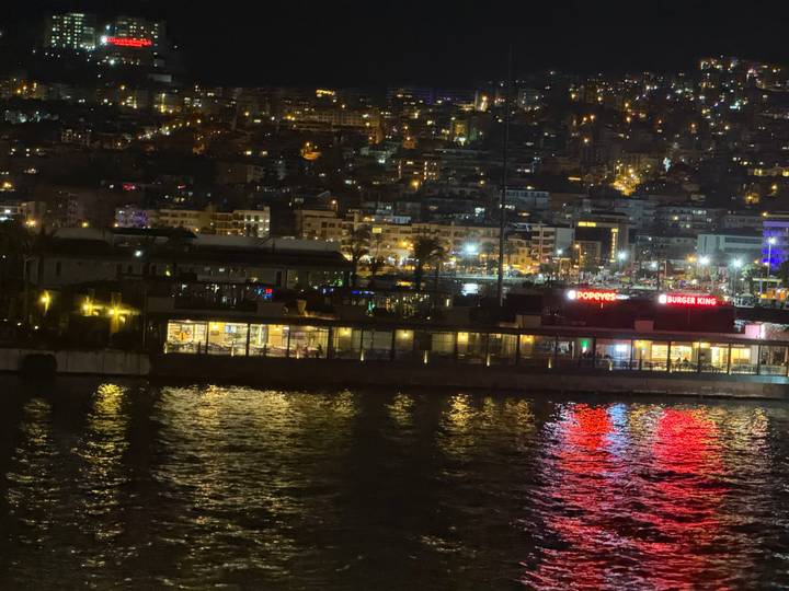 Vista nocturna de un paisaje urbano con letreros de restaurantes reflejándose en el agua.
