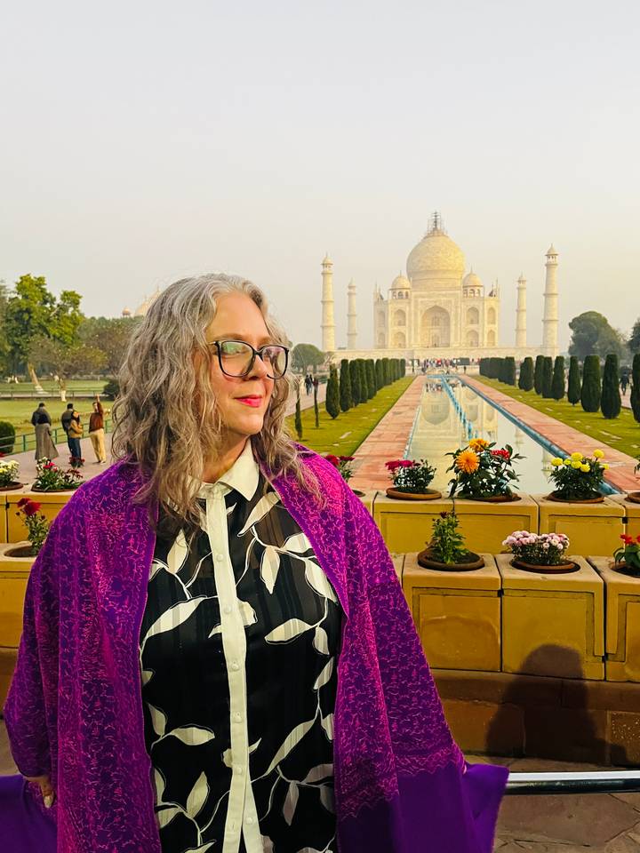 Persona posando frente al Taj Mahal con flores y sendero de jardín.
